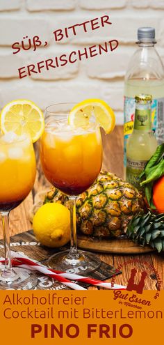 two glasses of alcohol sit on a table next to pineapples and oranges