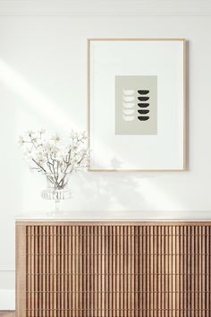 a vase with white flowers sitting on top of a wooden cabinet next to a painting