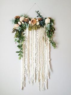 a white wall hanging with flowers and greenery on the top, along with other decorations