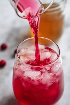 someone pouring red liquid into a glass filled with ice