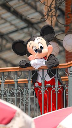 a mickey mouse statue standing on top of a metal railing next to a red and white umbrella