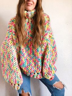 a woman wearing a multicolored sweater and ripped jeans is posing for the camera