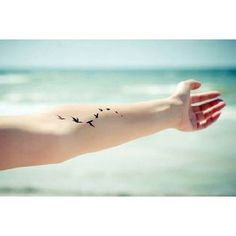 a woman's arm with birds flying over the ocean and beach in the background