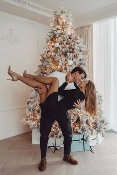 a man and woman dancing in front of a christmas tree