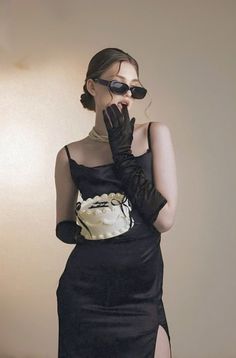 a woman in a black dress with her hands on her face, wearing gloves and sunglasses