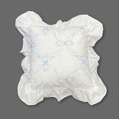 an embroidered pillow with ruffled edges and blue threadwork on the front, against a gray background