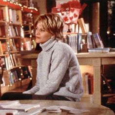 a woman sitting at a table in front of a bookshelf filled with books