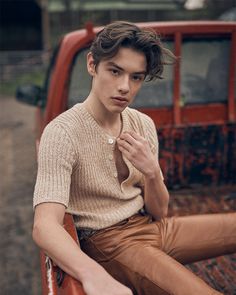 a young man sitting on the back of a truck wearing brown pants and a sweater