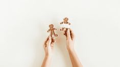 two hands holding small ginger cutouts in front of a white wall