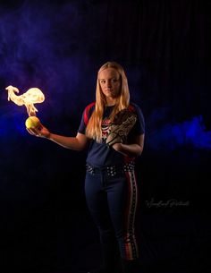 a woman holding a ball and glove in her right hand while standing against a dark background