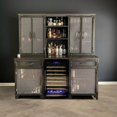 an open cabinet with bottles and glasses in it on the floor next to a wall