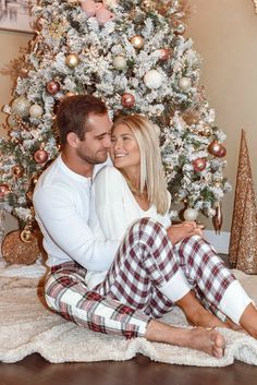 a man and woman sitting in front of a christmas tree