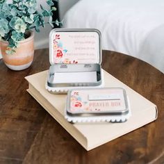 two tins sitting on top of a wooden table next to a potted plant