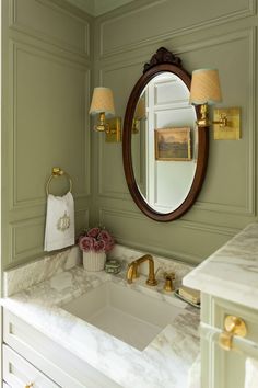 a bathroom with green walls and marble counter tops, gold faucet, white sink and large round mirror