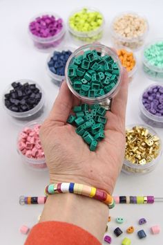 a hand holding a small container filled with beads and crayons next to other containers