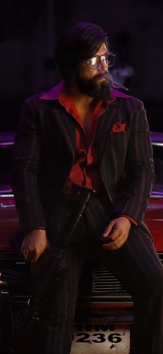 a man sitting on the hood of a car wearing glasses and a suit with a red shirt