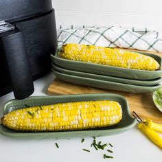 two corn cobs in green trays next to an air fryer