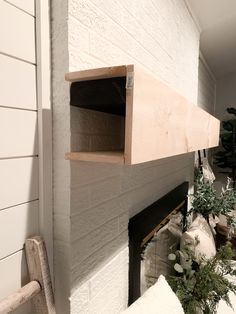 a white brick fireplace with two shelves on the wall and some plants in front of it