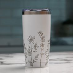 a white coffee cup with flowers on it sitting on top of a marble countertop