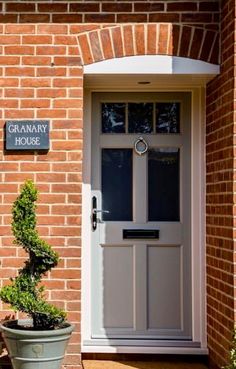 a white front door sitting next to a green potted plant on the side of a brick building