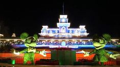 two large green plants are standing in front of a building with christmas lights on it