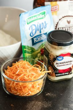 shredded carrots in a bowl next to dips and seasonings on a counter