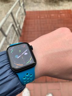 a person wearing a blue apple watch on their arm with a brick walkway in the background