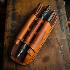 two pens in a leather case sitting on top of a wooden table