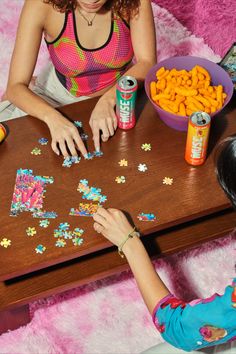 two girls are playing with puzzles on the table next to cans of soda and snacks