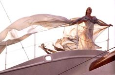 a woman is standing on the deck of a sailboat with her long flowing fabric