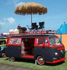 an old vw bus is parked on the grass with chairs and umbrella over it