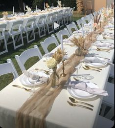 a long table set up with plates and silverware for an outdoor wedding reception in the grass