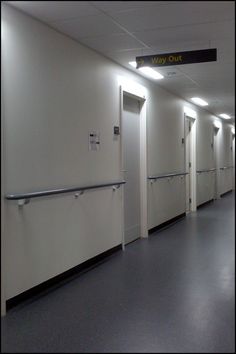 an empty hallway with white walls and metal railings on both sides, leading to the exit door