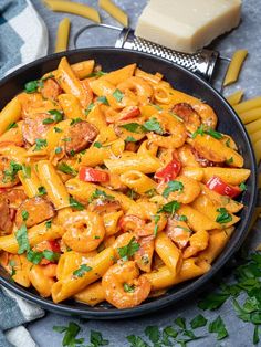 a skillet filled with pasta and sausage on top of a table next to cheese