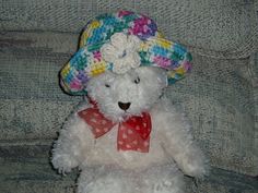 a white teddy bear with a colorful hat on it's head sitting on a couch