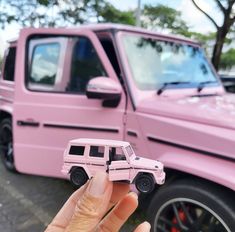 a hand holding a toy car in front of a pink truck