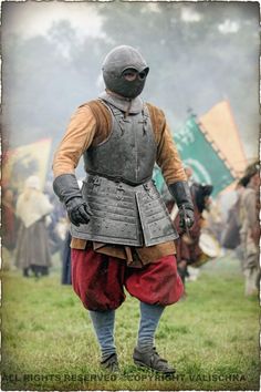 a man dressed in medieval clothing standing on top of a lush green field next to other people