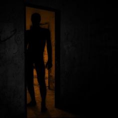 the silhouette of a man standing in an open doorway at night with his hands on his hips