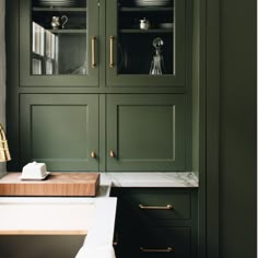 a kitchen with green cabinetry and marble counter tops, gold handles and brass pulls