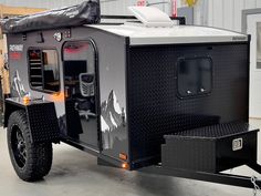 an off road camper trailer is parked in a garage with the door open and lights on