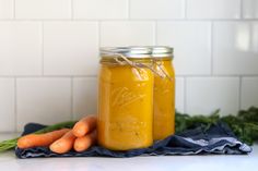 two jars filled with carrots sitting on top of a counter next to some vegetables