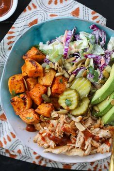 a bowl filled with chicken, coleslaw and sweet potato salad on top of a table