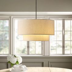 a light fixture hanging over a wooden table in a room with white flowers and windows