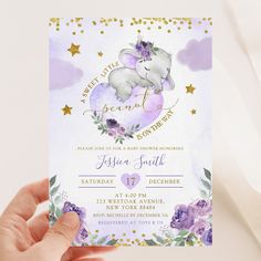 a person holding up a purple and gold elephant baby shower card with flowers on it