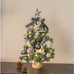 a small christmas tree with ornaments and lights on it's base, next to a pine cone