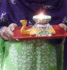 a woman holding a tray with a lit candle in it's center and a camel figurine on top