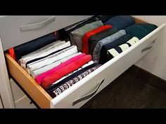 an open drawer filled with folded clothes on top of a wooden floor next to a white cabinet