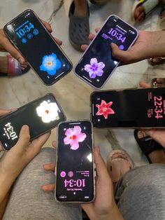 four people holding their cell phones in the middle of a circle with flowers on them