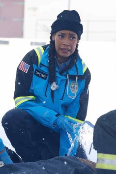 a woman in blue jacket and black hat sitting on snow covered ground next to fire hydrant