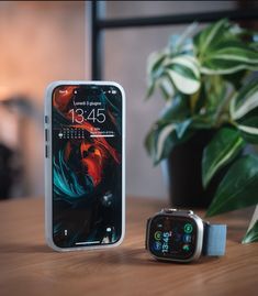 an apple watch sitting on top of a wooden table next to a cell phone and plant